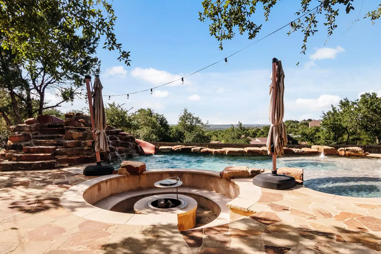 Pool with sunken round fire-pit seating, flagstone deck, boulder waterfall with red slide, umbrellas and string lights
