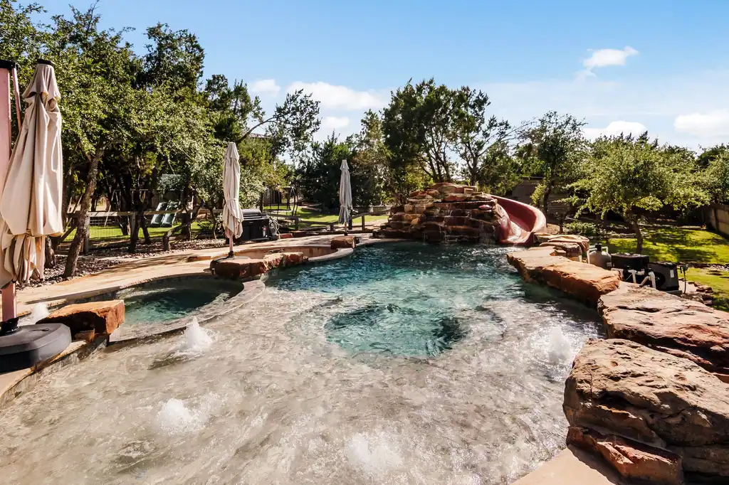 Pool with a rock waterfall, a slide, and fountain jets that Ridge Rock built at Canyonwood in Dripping Springs