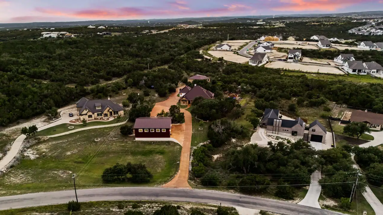 Dusk aerial from above a road of a red barn, an amber drive to a stone home and guest house, with neighboring homes