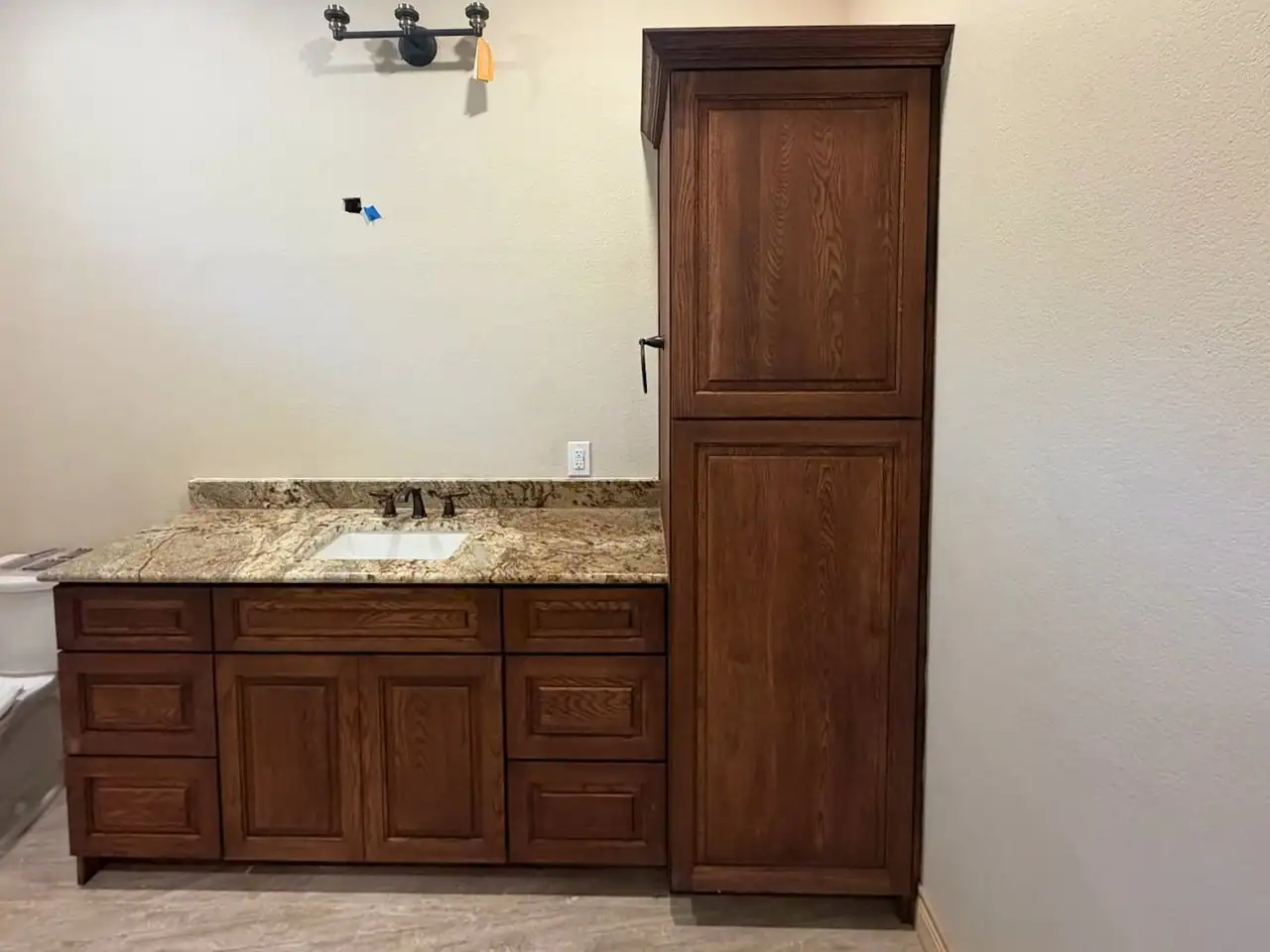 Bathroom with stained raised-panel vanity, matching tall linen cabinet, granite countertop, undermount sink and toilet