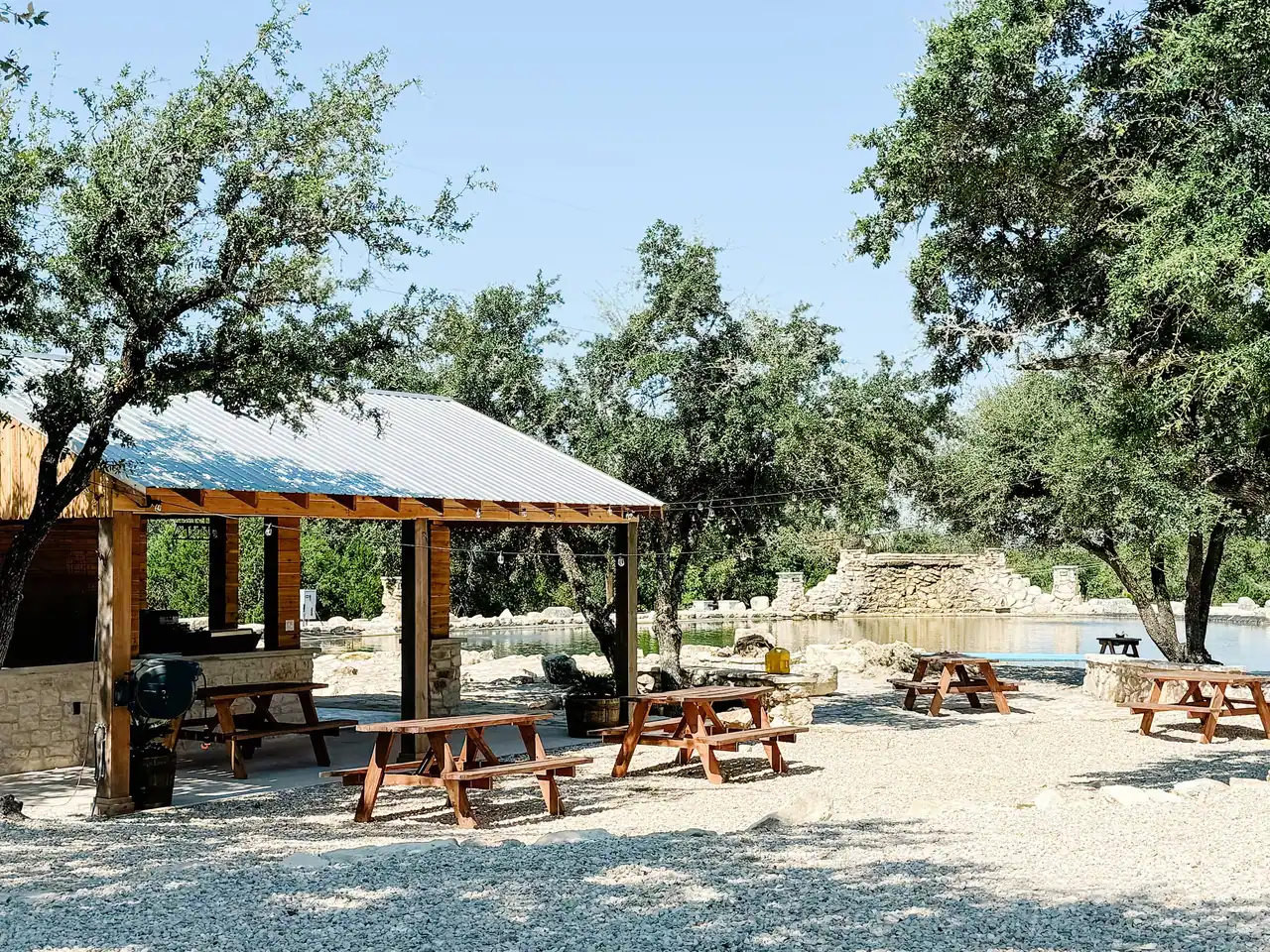 Timber pavilion with picnic tables beside the stone pool on the ranch