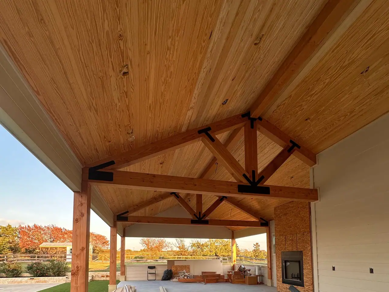 Cedar posts, timber trusses, and a wood plank ceiling over a pool cabana with a fireplace