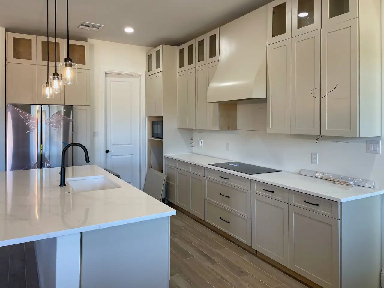 Finished kitchen with white cabinets, a large island, and pendant lights in a new Dripping Springs custom home