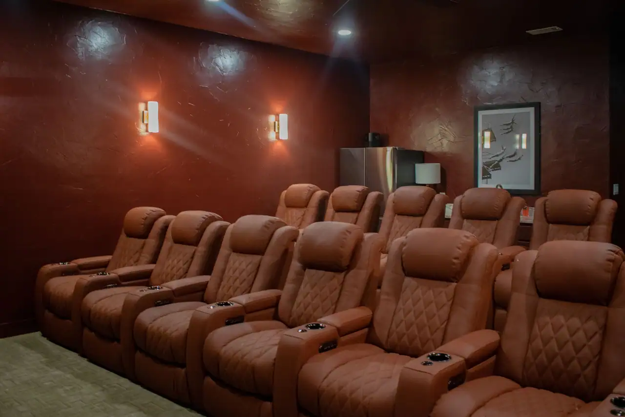 Home theater with rows of tan leather recliners, dark red textured walls, glowing wall sconces and framed art