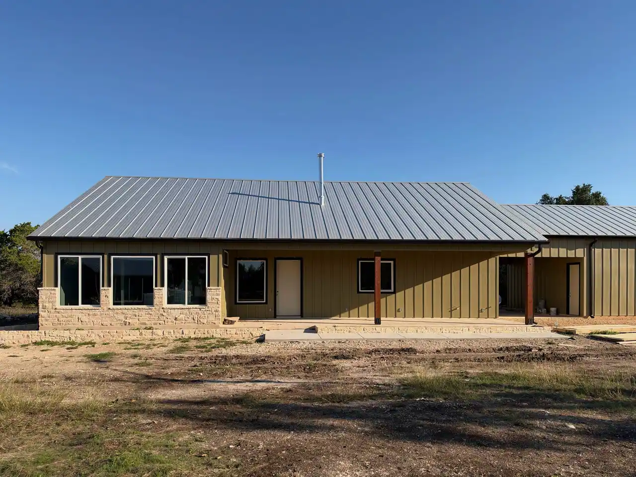 Custom home near completion in Liberty Hill with a stone wainscot, olive board-and-batten siding, a metal roof, and cedar porch posts