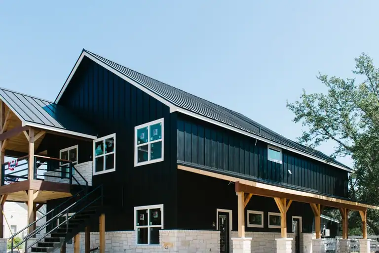 Two-story black board-and-batten barn with metal roof, stone base, timber-post porch and metal stair to a covered upper deck