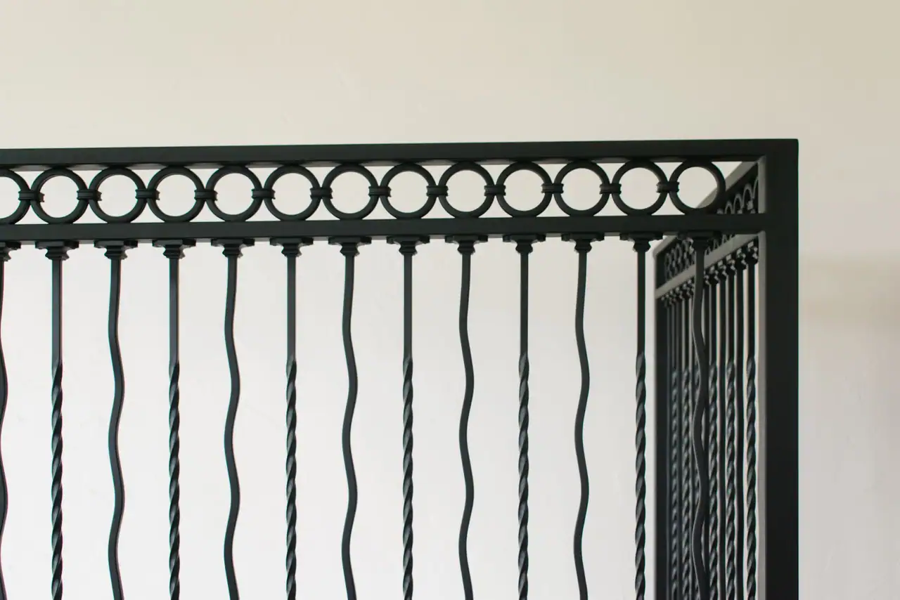 Top of a black iron railing with a band of rings over alternating twisted and wavy balusters
