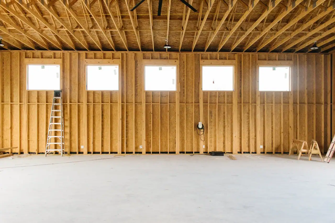 Red shop interior wall with five high windows, OSB sheathing, wood trusses, pendant lights and a bare slab floor