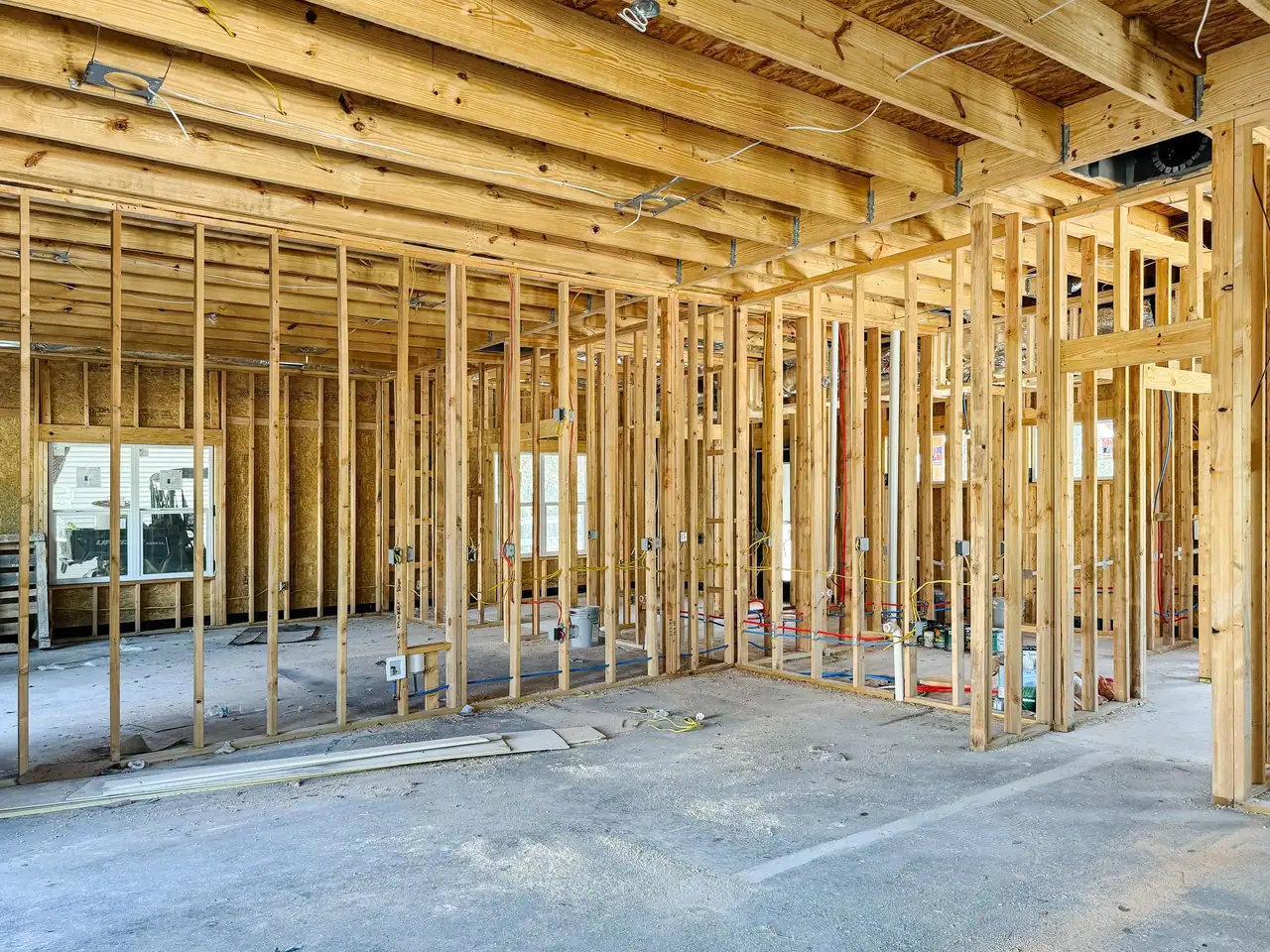 Stud partitions under floor joists, with electrical boxes, yellow and white wiring and red and blue supply lines on a slab