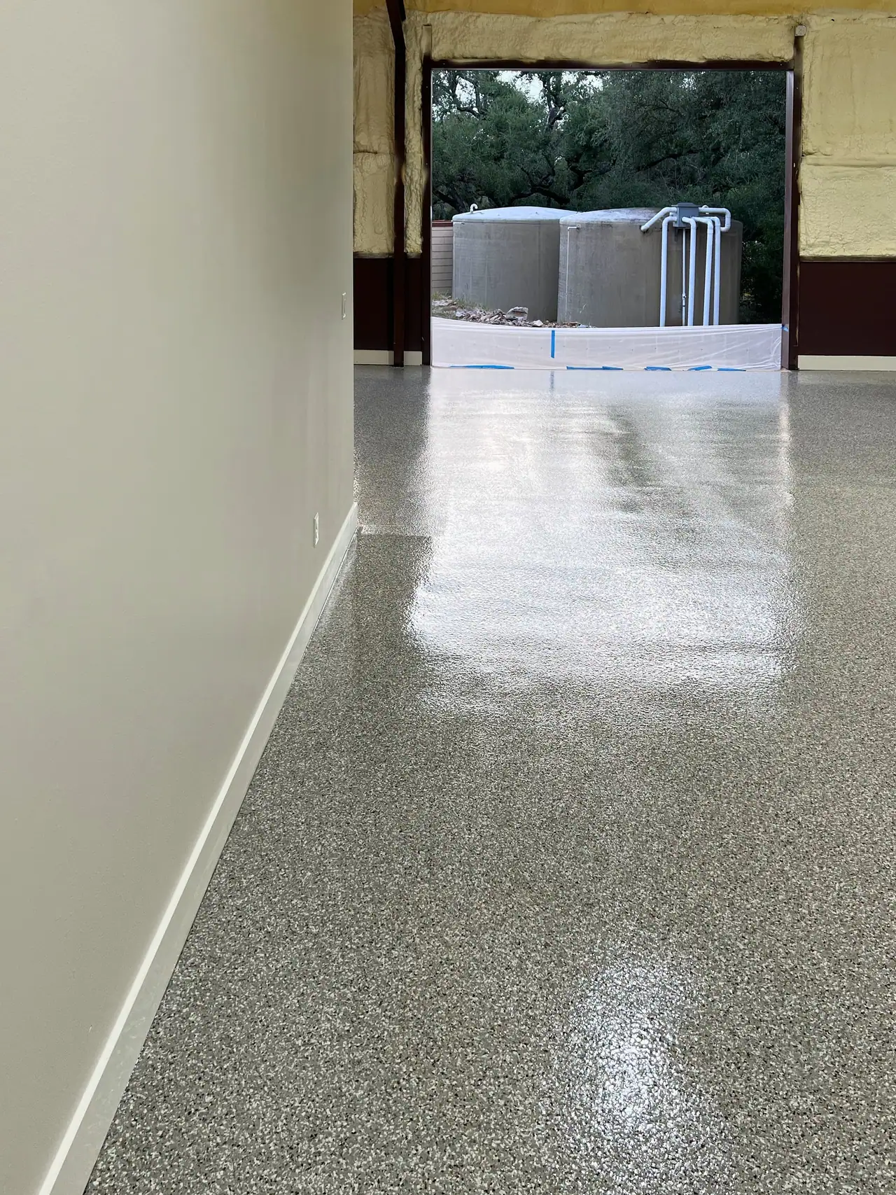 Glossy speckled flake floor coating along a hallway, looking out a wide opening to two large round tanks and trees