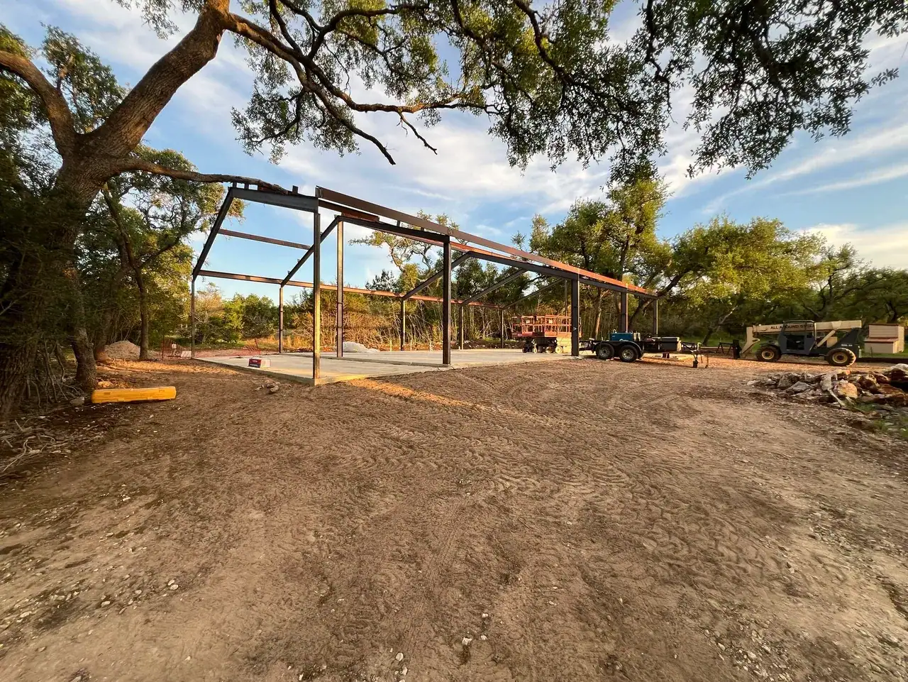 Steel building frame beneath mature oak trees during construction
