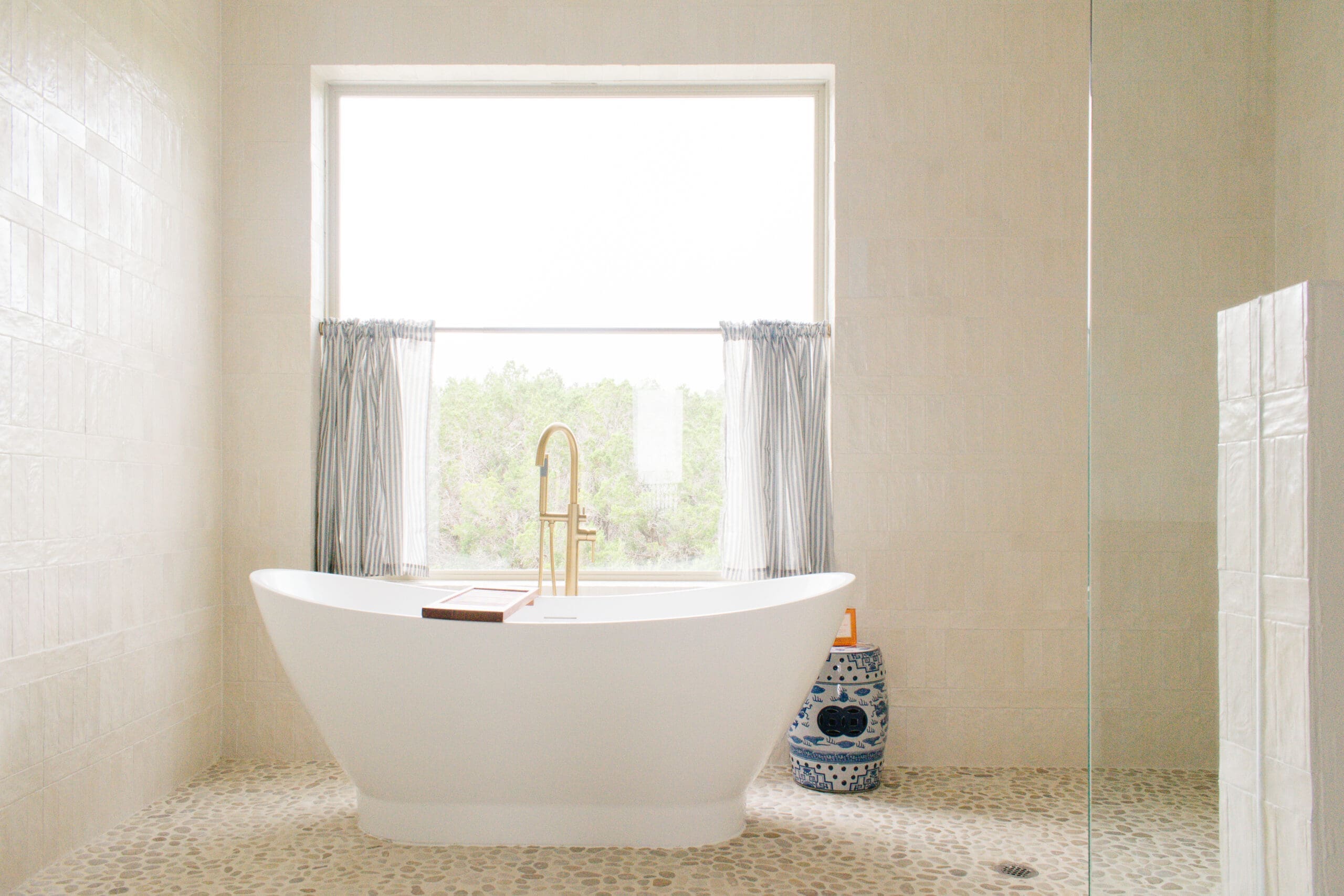 Remodeled bathroom with freestanding tub, brass fixtures, and a Hill Country window view by Ridge Rock Builders