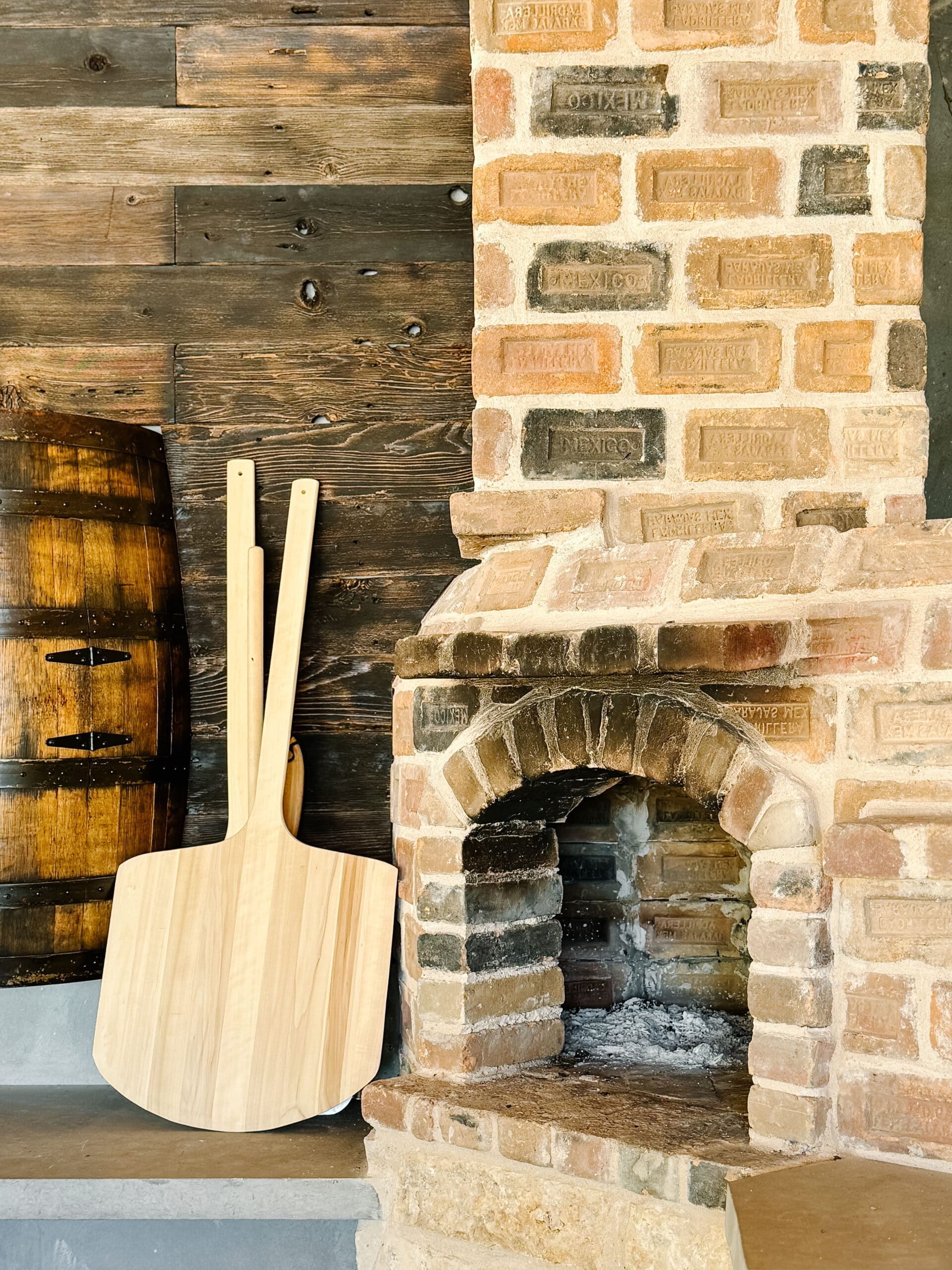 Stone wood-fired pizza oven with peels at an outdoor kitchen