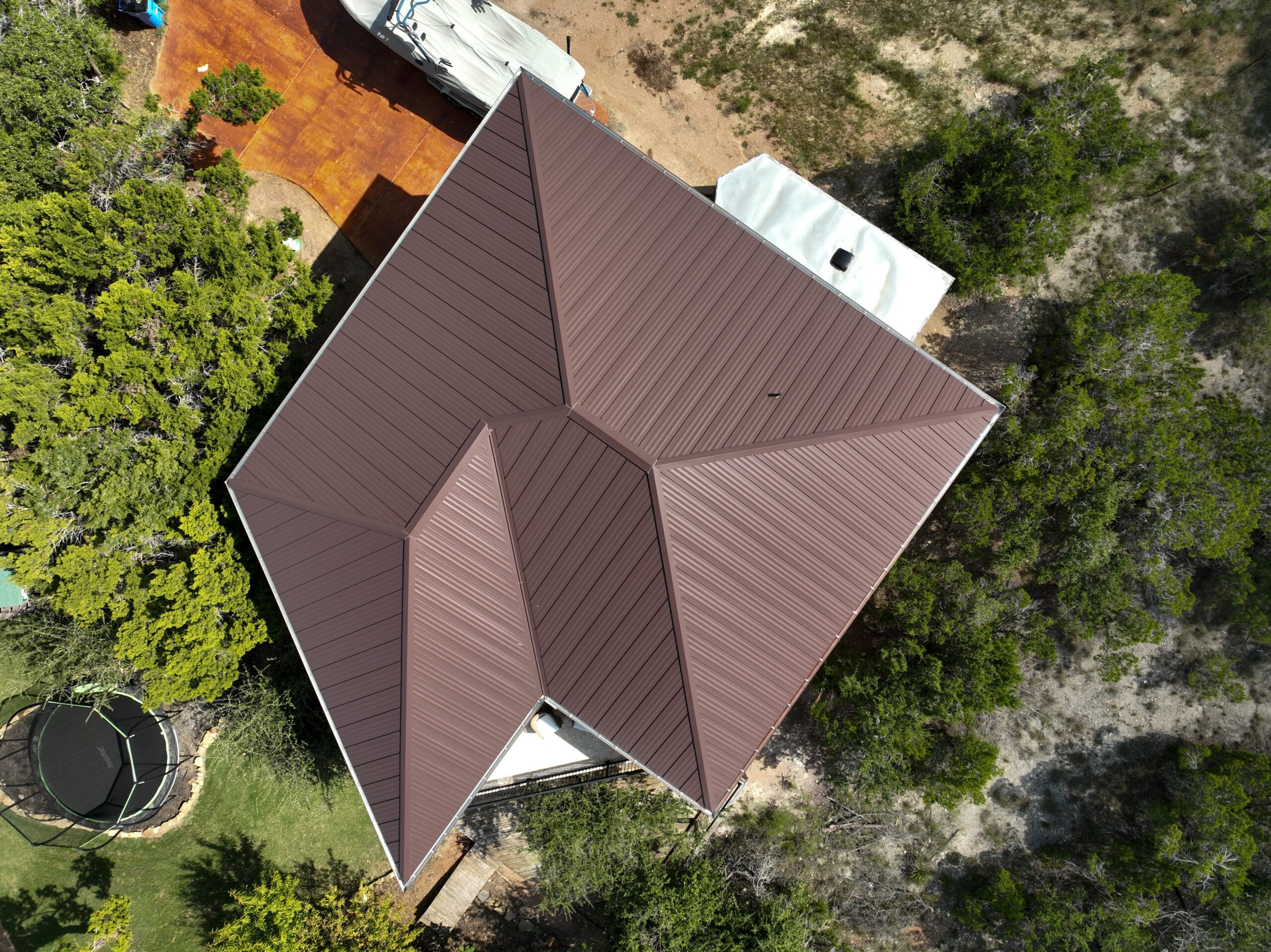 Aerial view of a metal-roofed custom home surrounded by oak trees