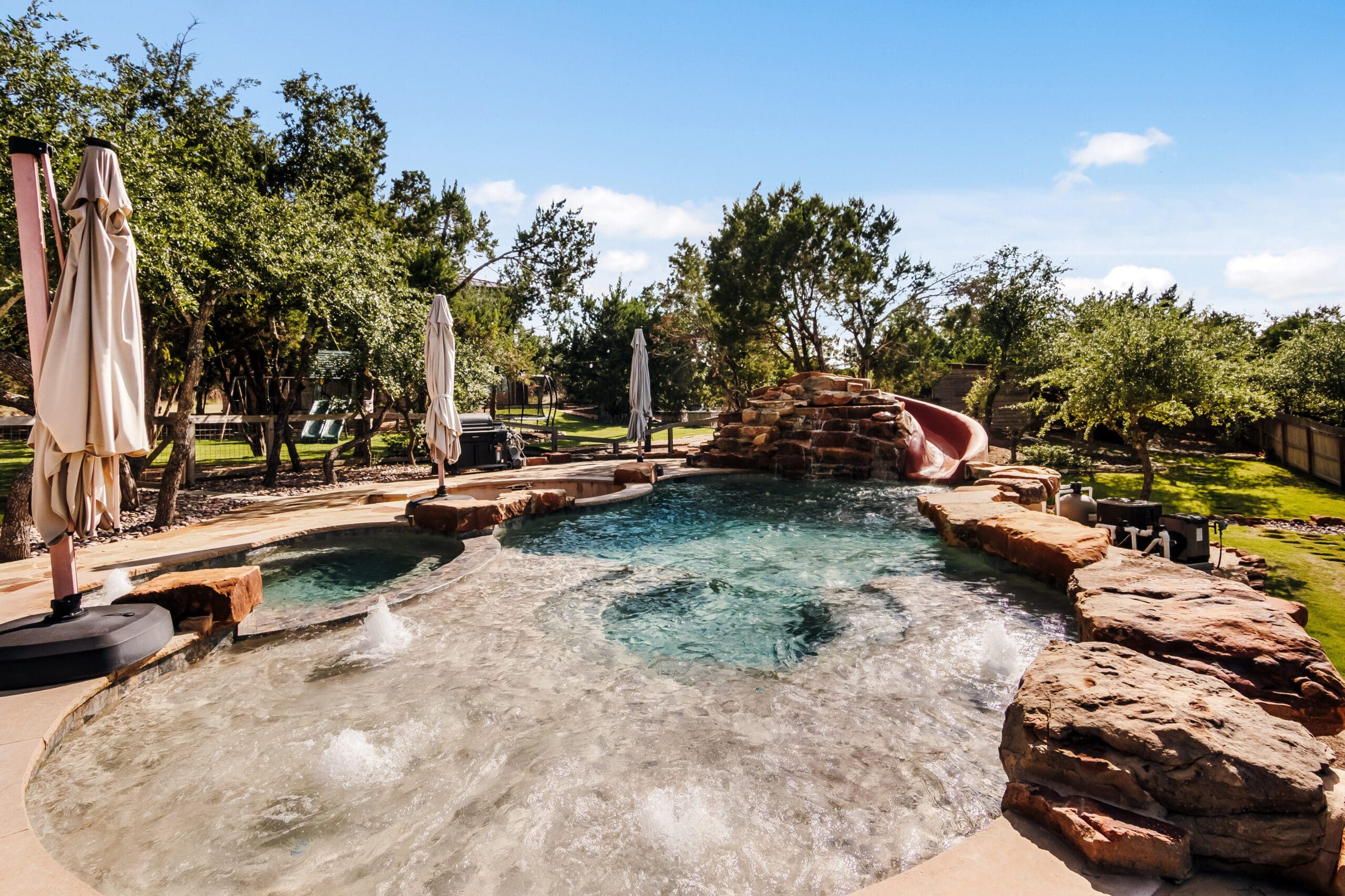 Custom pool with rock waterfall and slide in the backyard of a Dripping Springs home built by Ridge Rock Builders