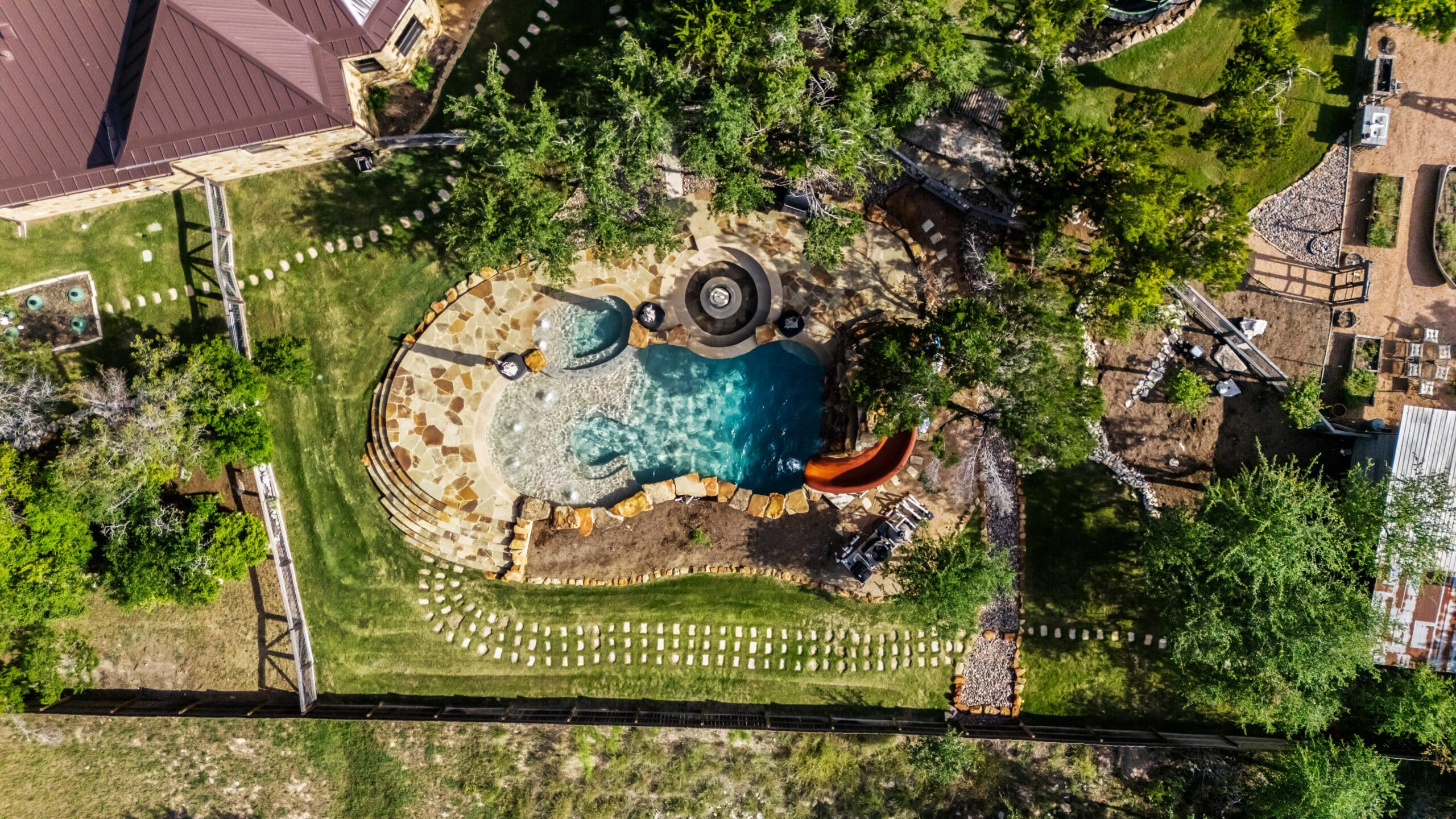 Aerial view of a custom rock pool with slide in a landscaped Dripping Springs backyard